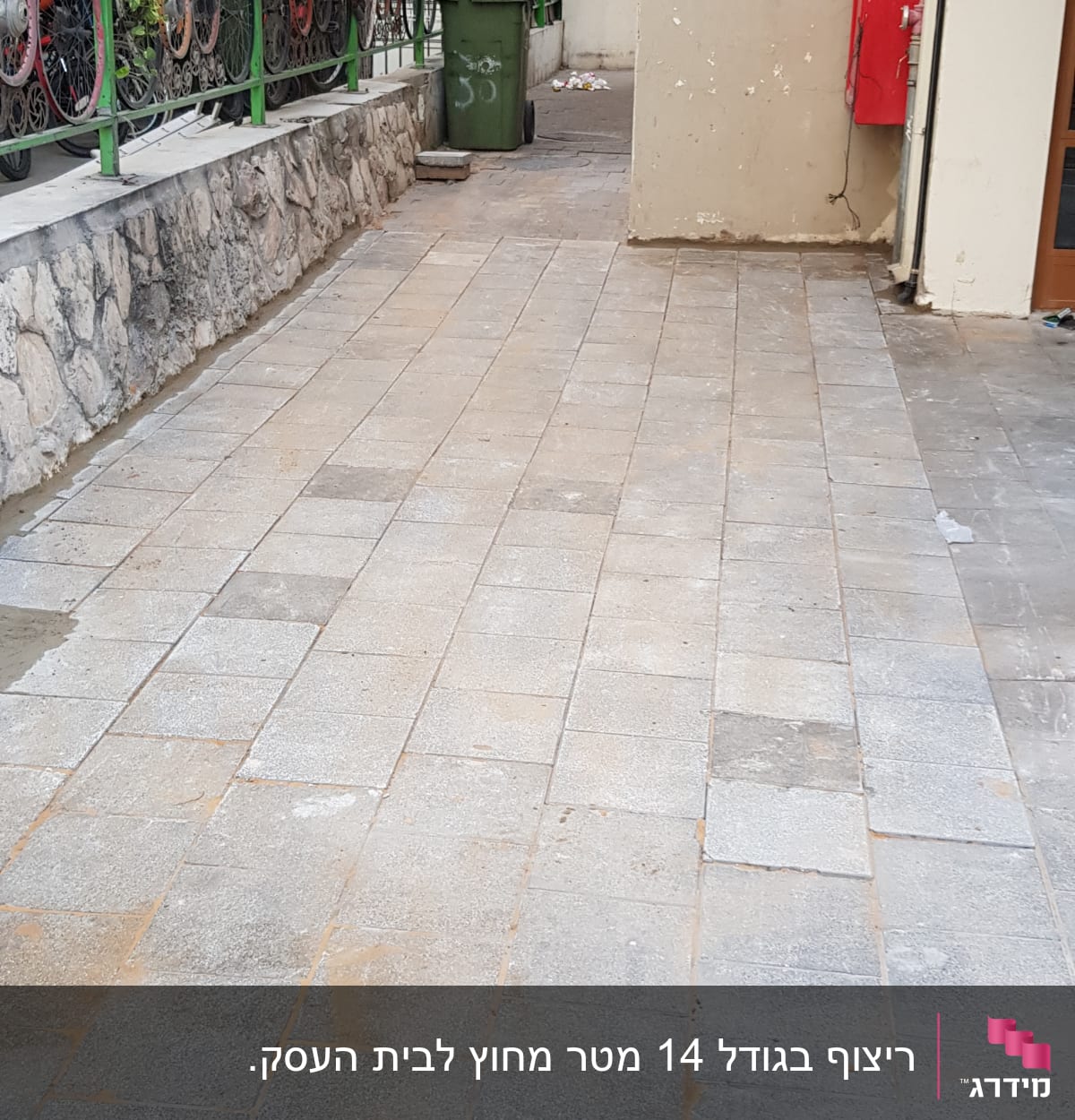 ריצוף חדש בחצר עם קיר אבן וגדר ירוקה